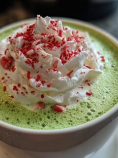 Close-up of a vibrant green Grinch Hot Chocolate topped with whipped cream and red sprinkles.