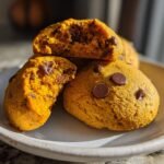 Close-up of soft, orange Milk Chocolate Jack O Lantern Cookies, one broken open to show the gooey interior.