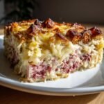 Close-up of a hearty slice of Reuben Bake casserole showing layers of corned beef, sauerkraut, and a cheesy topping.