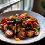 A close-up of a hearty Sausage Skillet featuring browned sausage slices mixed with saut&eacute;ed mushrooms, red, green, and yellow bell peppers.