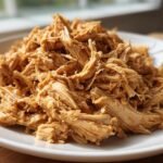 Close-up of perfectly shredded Crockpot Chicken piled high on a white plate.