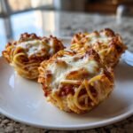 Three freshly baked Spaghetti Worm Cups topped with melted mozzarella cheese served on a white plate.
