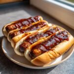 Four delicious Sticky Finger Hot Dogs smothered in thick, glossy BBQ sauce, served on a white plate.