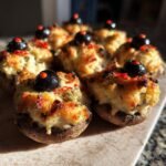 Close-up of baked Stuffed Mushroom Eyeballs topped with a black olive and red pepper garnish.