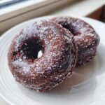 Close-up of two rich, dark chocolate doughnuts heavily coated in sparkling granulated sugar.