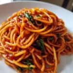 A close-up, appetizing shot of spaghetti coated in rich red Tomato Pasta sauce and garnished with fresh basil leaves.