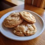 A stack of four soft, golden White Chocolate Maple Cookies with visible melted white chocolate chips on a small white plate.