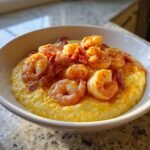 A close-up view of creamy, yellow Shrimp Grits Bowls topped with seasoned shrimp and crispy bacon pieces.