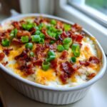 Close-up of a creamy Baked Potato Dip topped with melted cheddar cheese, crispy bacon bits, and fresh green onions.