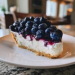 A close-up of a perfect slice of Blueberry Cream Cheese Pie featuring a thick cream cheese layer and topped generously with fresh blueberries and glaze.