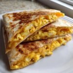 Close-up of stacked, toasted Breakfast Quesadilla wedges filled with fluffy scrambled eggs and melted cheese.