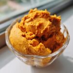A close-up, brightly lit serving of rich orange Pumpkin Mousse scooped into a small, clear glass bowl.