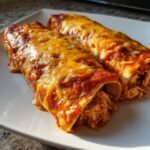 Close-up of two freshly baked Chicken Enchiladas covered in melted orange cheese and red sauce.