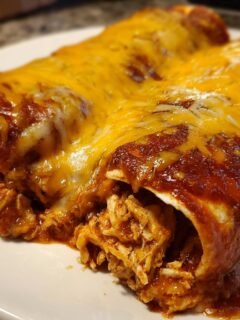 Close-up of two saucy Chicken Enchiladas topped with melted cheddar cheese, showing shredded chicken filling.
