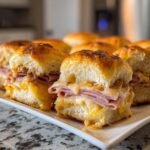 Close-up of freshly baked Club Sliders filled with melted cheese and layers of sliced ham on a white serving tray.
