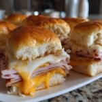 Close-up of several baked Club Sliders with melted white and orange cheese oozing over layers of ham.