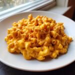 A close-up of creamy Buffalo Mac And Cheese with visible shredded chicken mixed into the bright orange sauce.