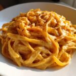 A close-up of creamy Pumpkin Alfredo Pasta tossed with fettuccine, garnished with pepper flakes.