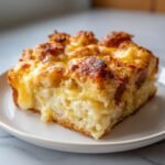 Close-up of a square serving of warm Croissant Breakfast Casserole with melted, golden-brown cheese topping.