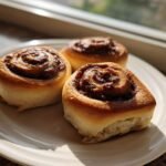 Three golden-brown Nutella Rolls with gooey centers sitting on a white plate near a sunny window.