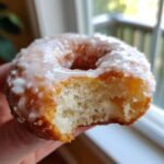 Close-up of a fluffy, glazed Apple Donuts with a bite removed, showing the soft interior texture.