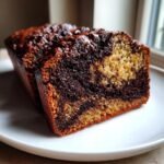 A close-up of a thick slice of Hot Fudge Brownie Bread showing a rich, dark chocolate swirl next to the lighter batter.