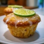 A close-up of a moist Margarita Cupcakes topped with a sweet glaze and a thin slice of fresh lime.