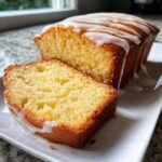 Close-up of a slice of moist Lemon Bread next to the loaf, drizzled with white icing.
