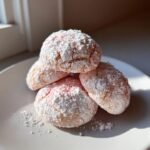 A stack of four pink Strawberry Cookies heavily dusted with powdered sugar resting on a white plate.
