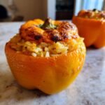 Close-up of a baked orange Pumpkin Stuffed Peppers filled with seasoned rice and a slightly browned cheesy top.