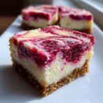 A close-up of one square of Raspberry Cheesecake Bars showing a thick graham cracker crust and a creamy, swirled raspberry topping.