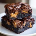 Two rich, fudgy Reeses Brownies stacked, showing melted peanut butter cups inside the dark chocolate.