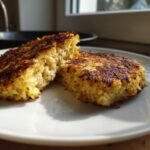 Two golden brown Cabbage Burgers, one cut open to show the texture, resting on a white plate.