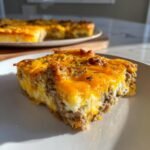 A close-up of a hearty slice of 12-Egg Bake featuring layers of sausage, eggs, and melted cheddar cheese.