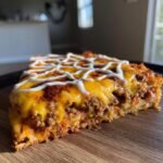 A thick slice of Spiderweb Taco Pizza featuring a ground meat layer, melted cheddar cheese, and a sour cream drizzle.