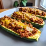 Three baked Stuffed Zucchini Boats filled with savory ground meat and topped with melted cheddar cheese.