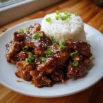 Close-up of glossy Teriyaki Chicken and Rice topped with sesame seeds and green onions.