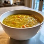 Close-up of a white bowl filled with thick, hearty Split Pea Soup featuring visible chunks of orange carrots.