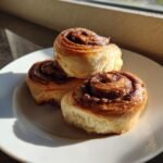 Three freshly baked Nutella Rolls stacked on a white plate, illuminated by bright sunlight.