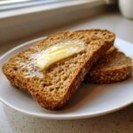 Two slices of toasted Ezekiel Bread topped with a melting pat of butter and honey.