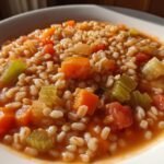 Close-up of a hearty bowl of Vegetable Barley Soup featuring plump barley, diced carrots, celery, and tomatoes in a rich broth.
