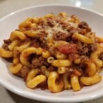 A close-up shot of a hearty serving of Beef Macaroni mixed with ground beef and tomato sauce, topped with melted cheese.