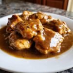 Close-up of tender chicken pieces smothered in rich, dark brown gravy, ready to eat. Perfect Chicken And Gravy.