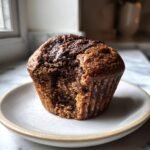 A close-up of a Chocolate Swirl Muffins with a bite taken out, showing the marbled interior.