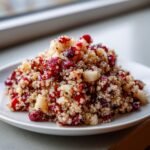 A close-up shot of a serving of Cranberry Apple Quinoa Salad featuring fluffy quinoa, dried cranberries, and diced apples on a white plate.