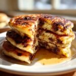 Close-up of a stack of fluffy Chocolate Chip Pancakes with a slice cut out, drizzled with syrup.