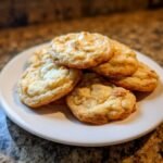 A stack of freshly baked, golden Cake Mix Cookies with visible white chocolate chunks on a white plate.