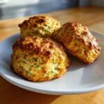 Three freshly baked Zucchini Scones with golden, craggy tops resting on a white plate.
