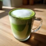 A vibrant green Matcha Latte with thick white foam, layered over milk in a clear glass mug.