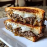Two halves of a delicious Patty Melts sandwich stacked, showing melted cheese, ground beef, and caramelized onions between toasted bread.